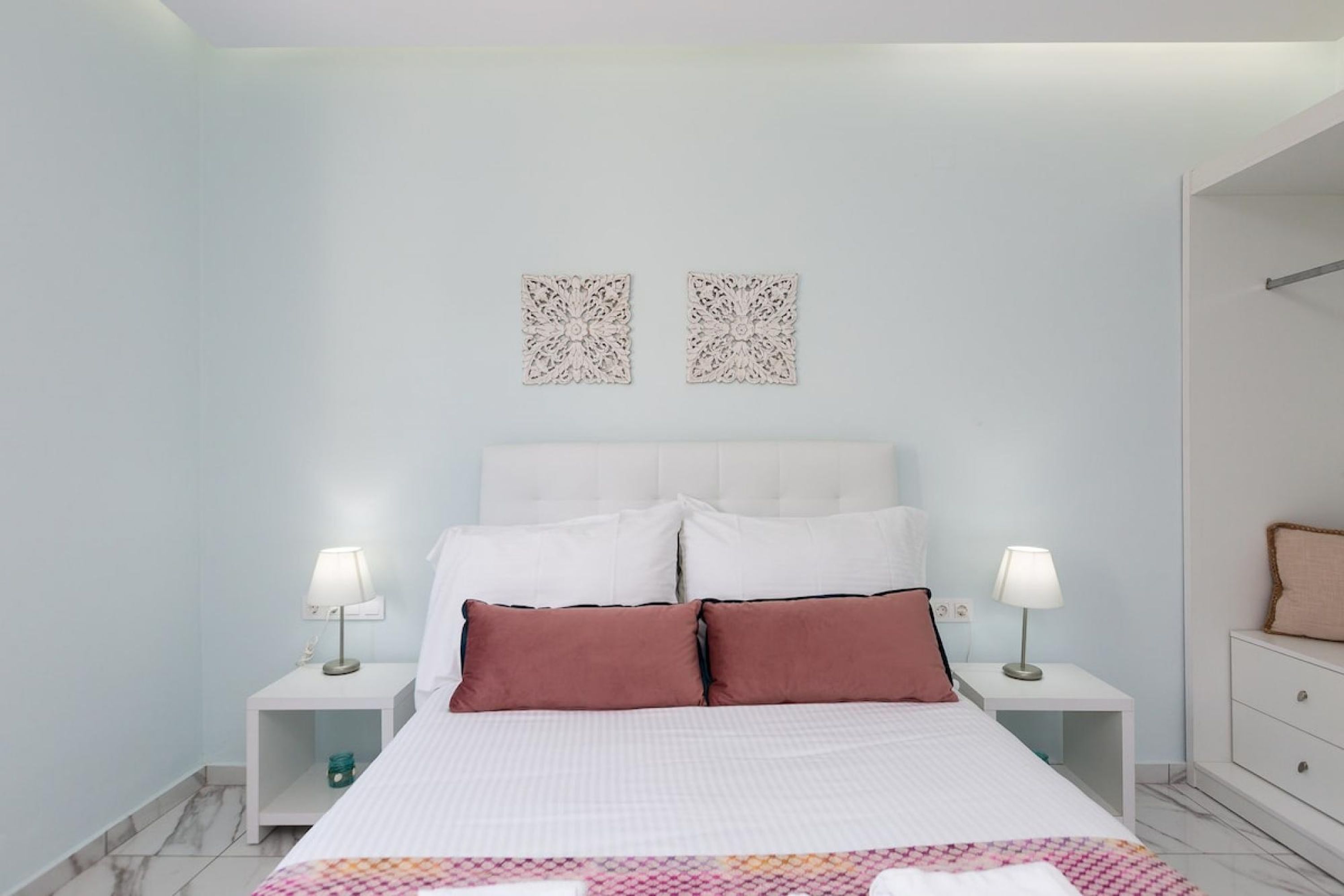 Un dormitorio con una cama, dos mesitas de noche, un aparador y dos adornos en la pared.