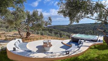 Un jacuzzi con zona de estar circular, rodeado por una valla y árboles, con vistas a un paisaje montañoso.