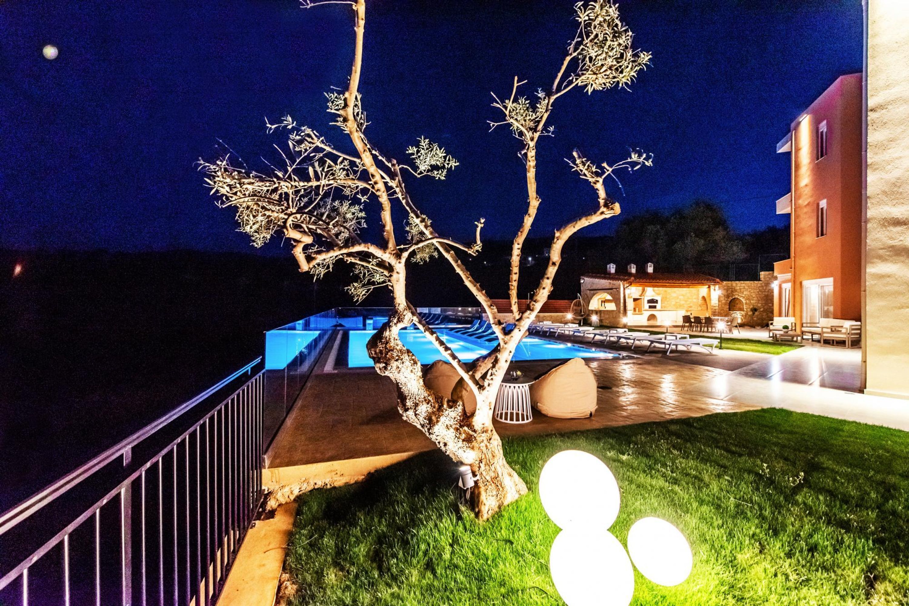 Ein Hotel bei Nacht mit Swimmingpool, einer gut beleuchteten Baum und einer Rasenfläche.