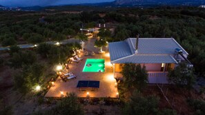 A house with a swimming pool, outdoor seating, and a well-lit patio area surrounded by trees. - Villa Avra - With Private Pool (Mylopotamos)