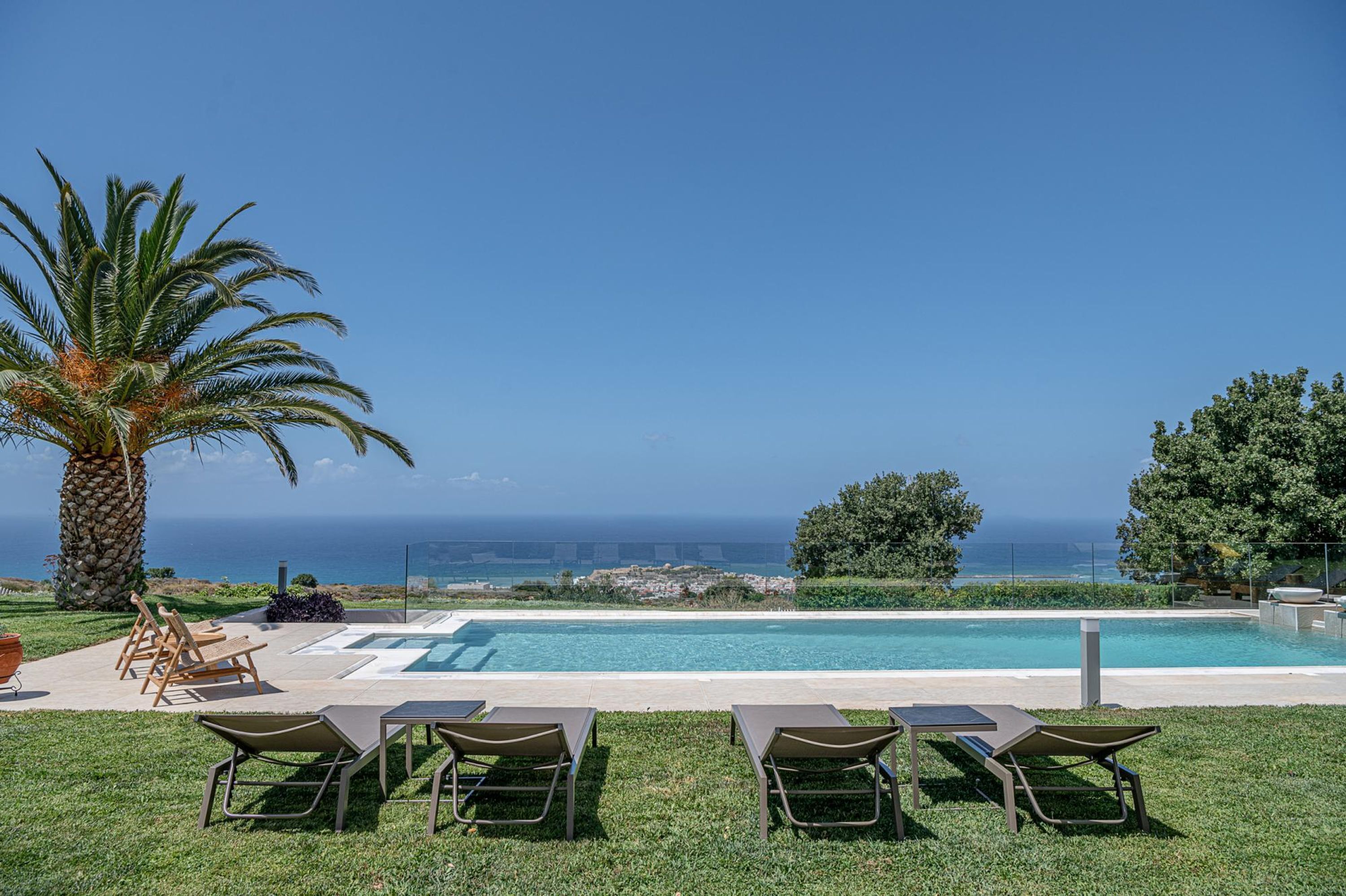 A pool area with lounge chairs and a palm tree, overlooking a scenic view of the ocean and a bridge.