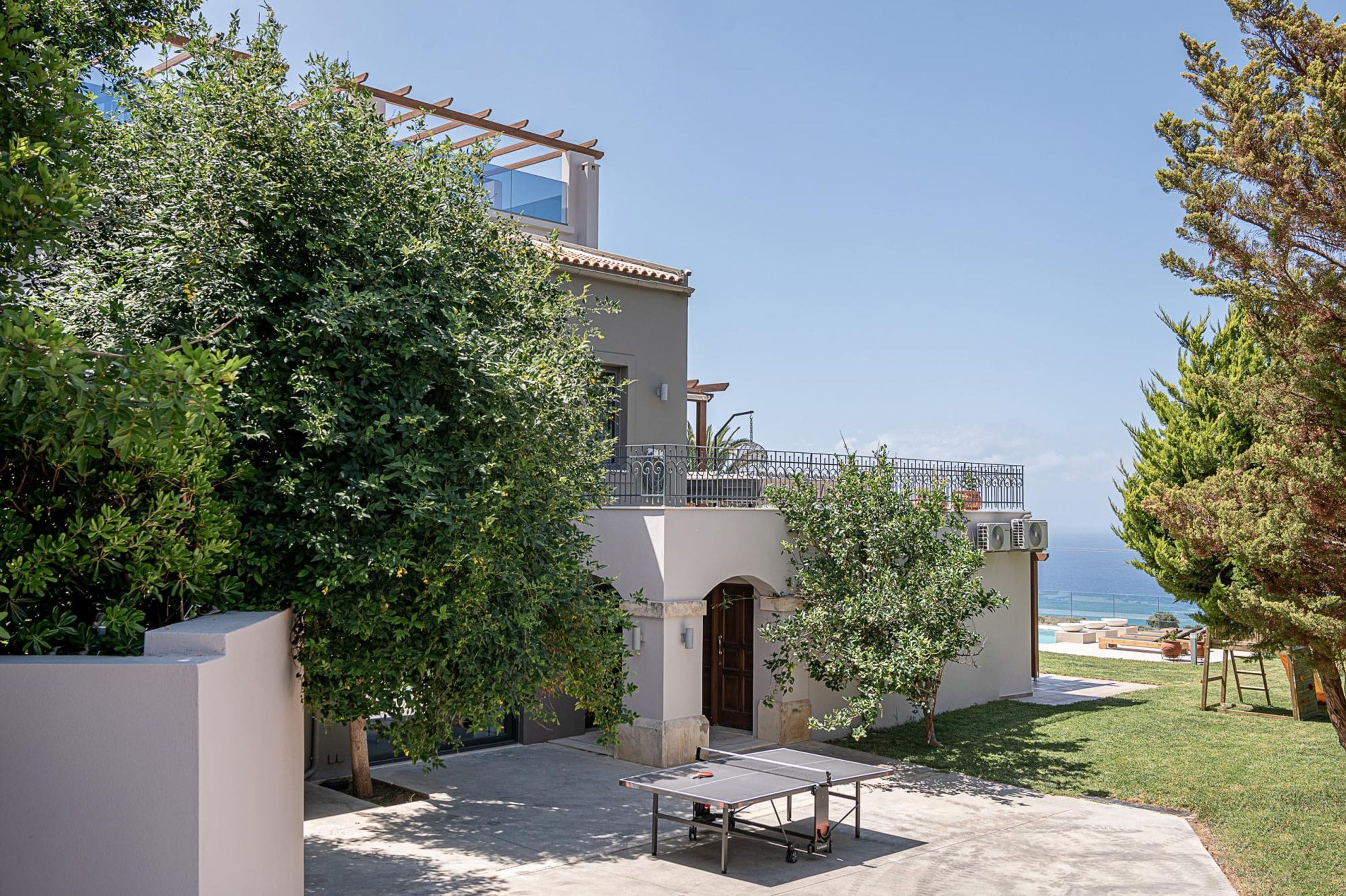 A modern building with a balcony overlooking the sea, surrounded by greenery.