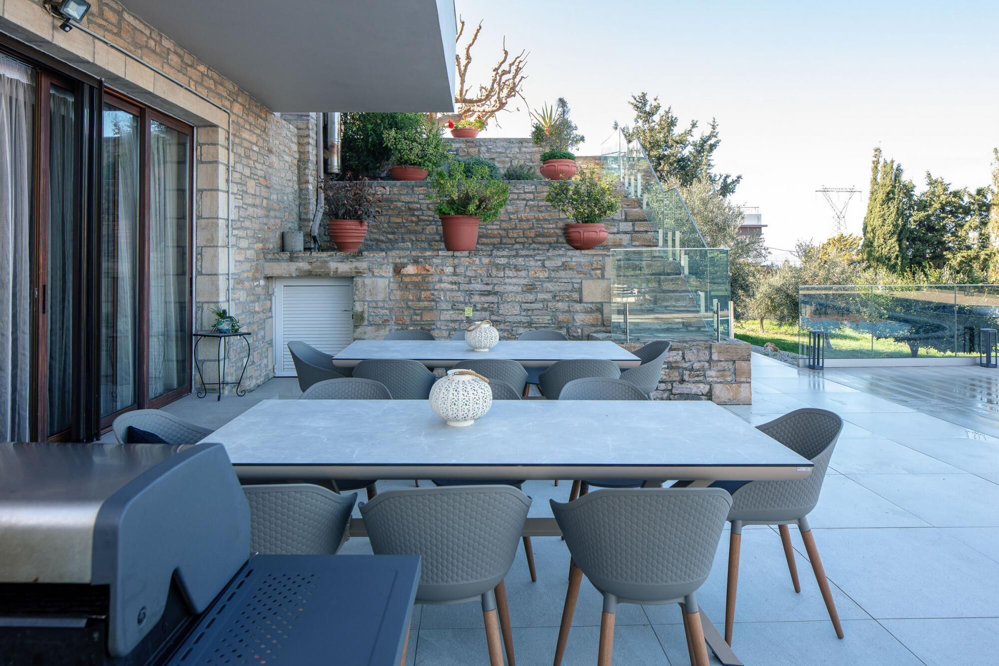Une terrasse extérieure avec un mur en pierre, une rambarde en verre et une table entourée de chaises.