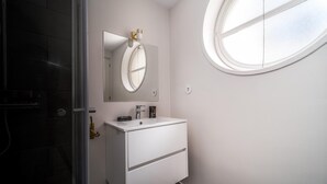 A bathroom with a white vanity, a round mirror, and a window. - Nomad s By Sta Catarina Flats - 3bed Moments (Porto)