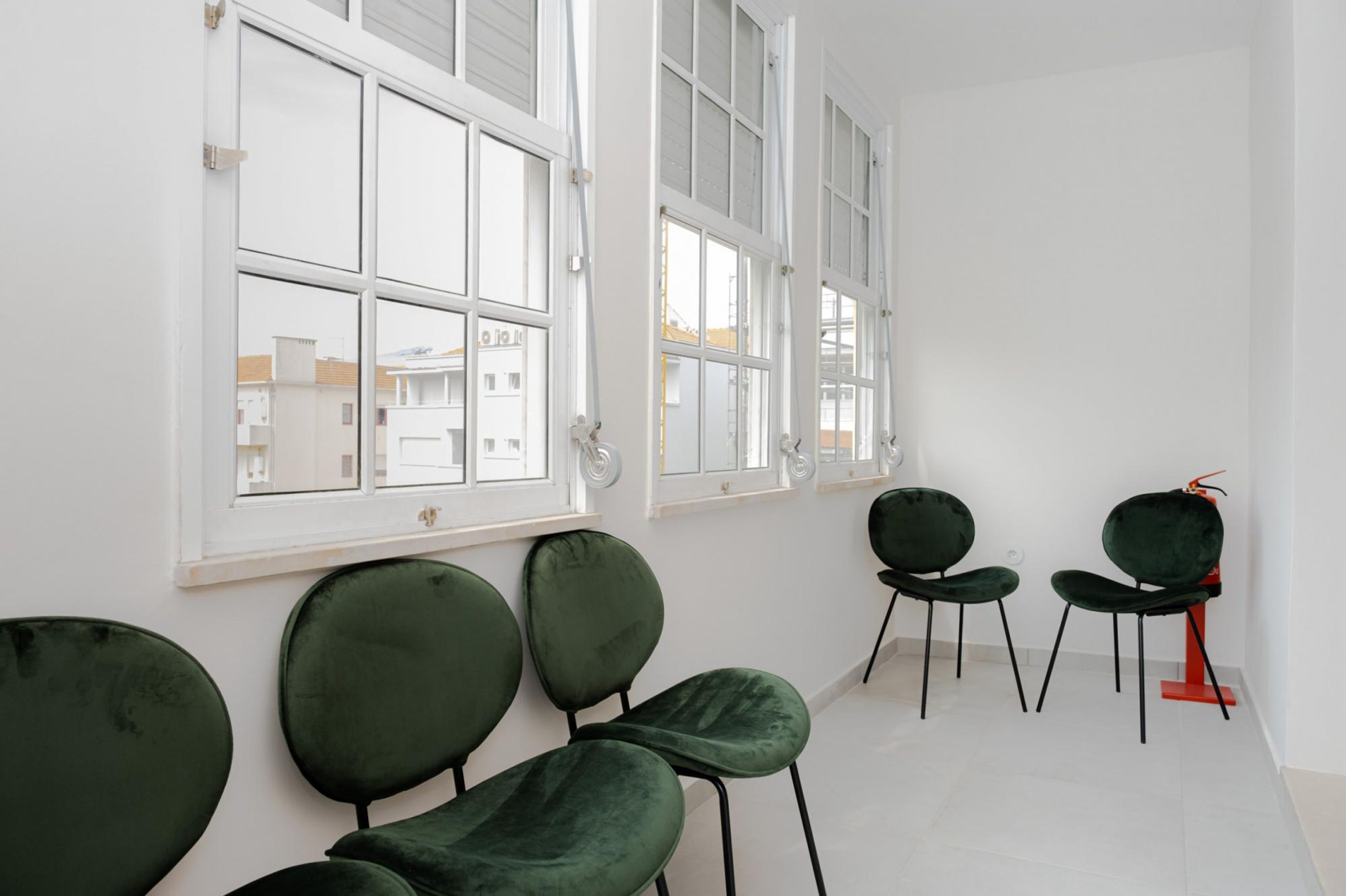 A room with large windows, green chairs, and a red chair.