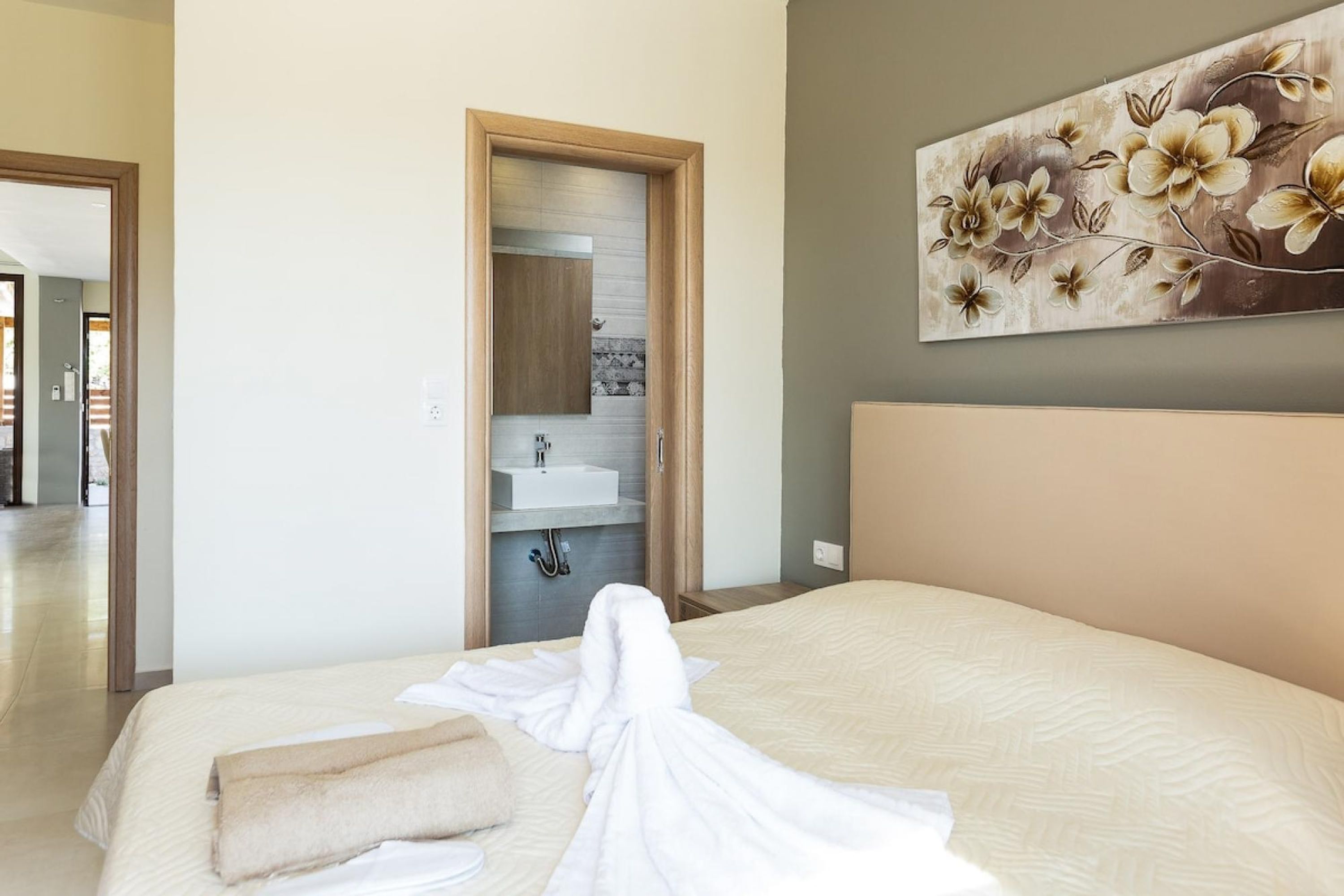 A hotel room with a bed, a bathroom with a sink, and a painting on the wall.