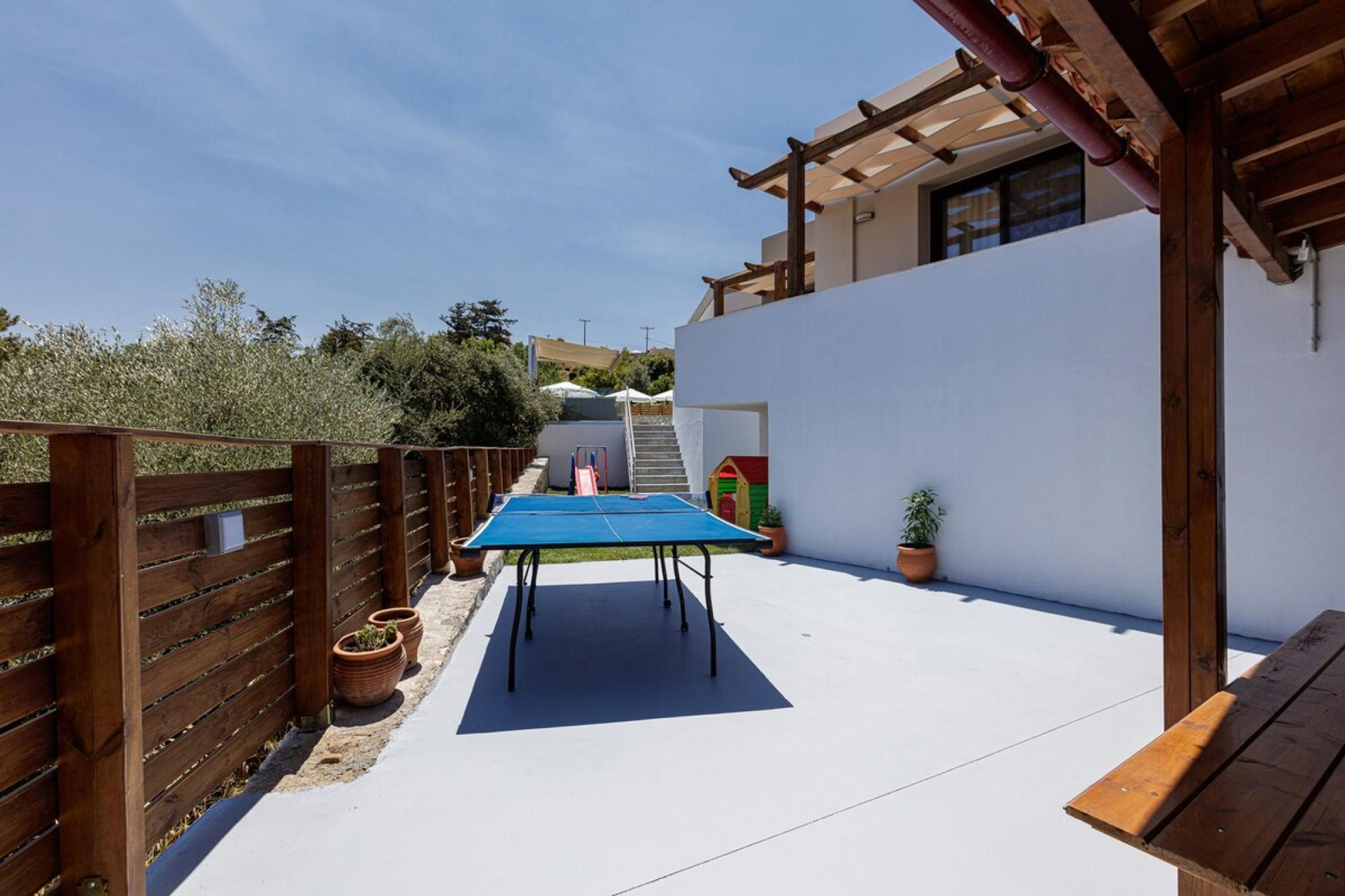 An outdoor patio with a ping pong table, wooden fence, and potted plants.