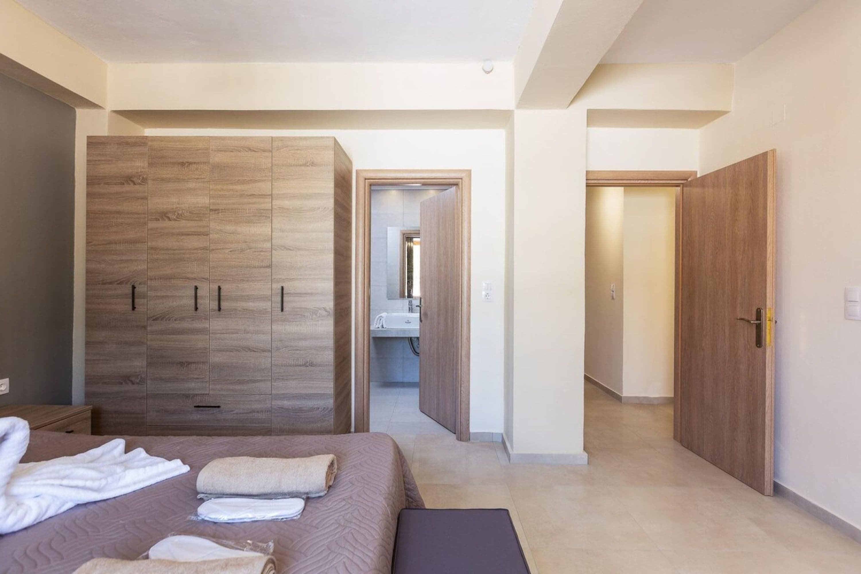 A modern bedroom with a large wardrobe, a neatly made bed, and a bathroom visible through an open door.