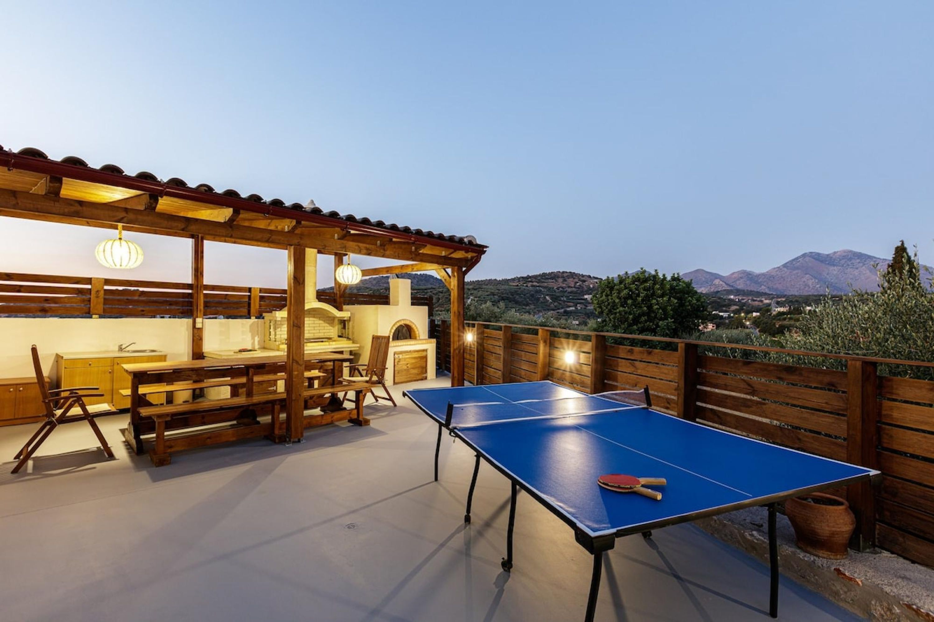 An outdoor dining area with a ping pong table, wooden furniture, and a view of the mountains.