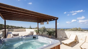 Een dakterras met een hottub, lounge stoelen en een pergola.
