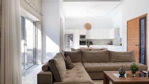 Een moderne woonkamer met een hoekbank, een houten salontafel en uitzicht op een keuken en eetgedeelte.