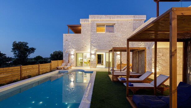Een modern huis met een zwembad, buitenmeubilair en een gevel van natuursteen.