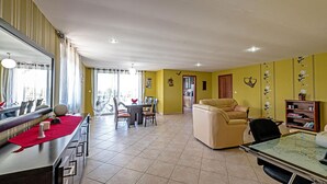 A spacious living area with a dining table, a sofa, and a large window. - Villa Guinevere-with Private Pool (Rethymno)