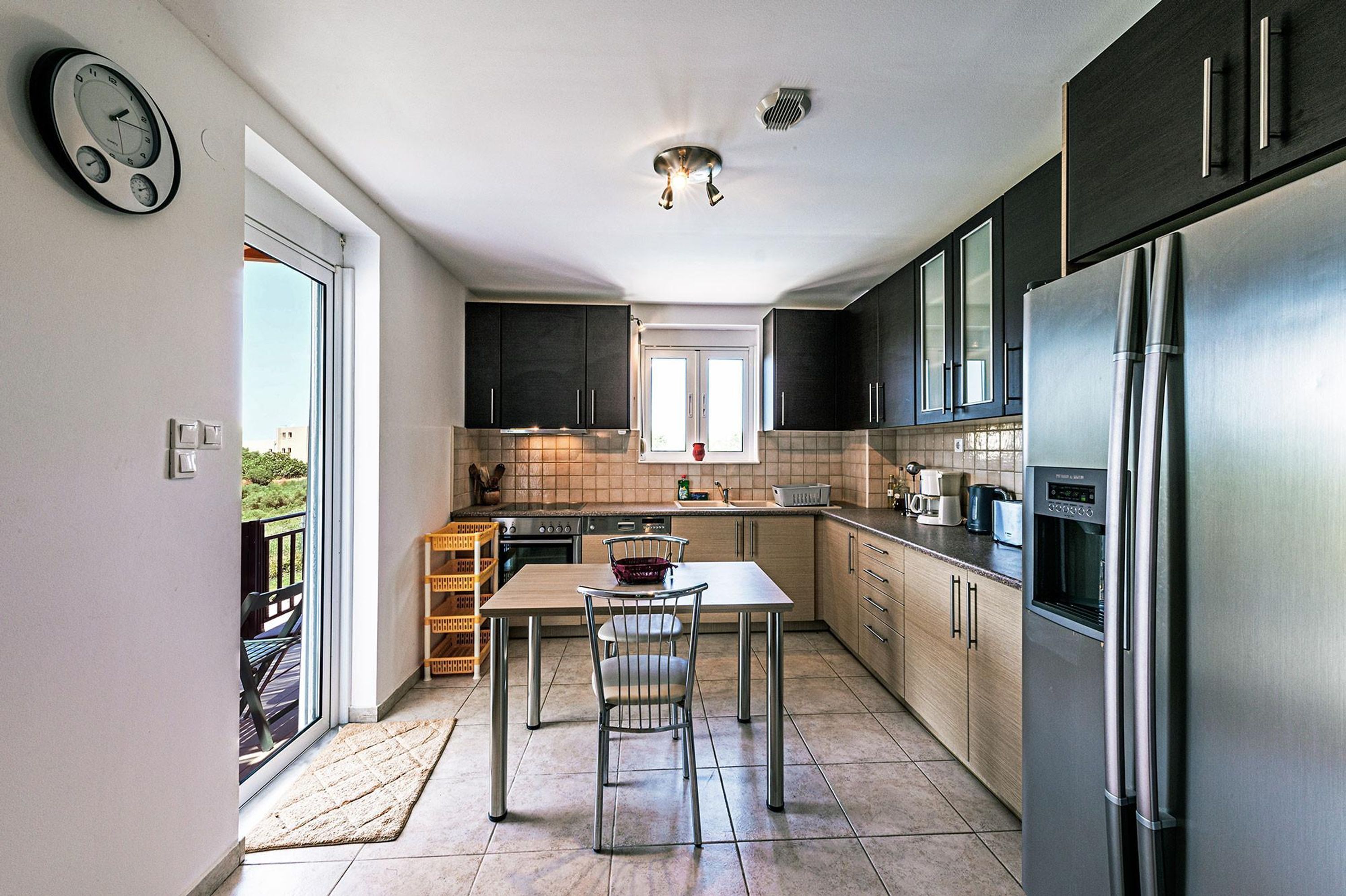 A modern kitchen with a stainless steel refrigerator, dark cabinets, and a window overlooking a balcony.