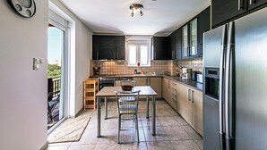 A modern kitchen with a stainless steel refrigerator, dark cabinets, and a window overlooking a balcony. - Villa Guinevere-with Private Pool (Rethymno)