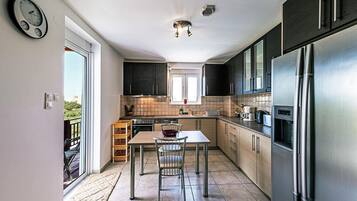 A modern kitchen with a stainless steel refrigerator, dark cabinets, and a window overlooking a balcony.