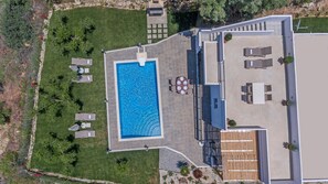 An aerial view of a modern house with a rectangular swimming pool, outdoor seating area, and a patio with a pergola.