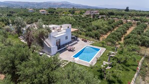 A modern two-story house with a swimming pool, surrounded by lush greenery and a hilly landscape. - Villa Guinevere-with Private Pool (Rethymno)