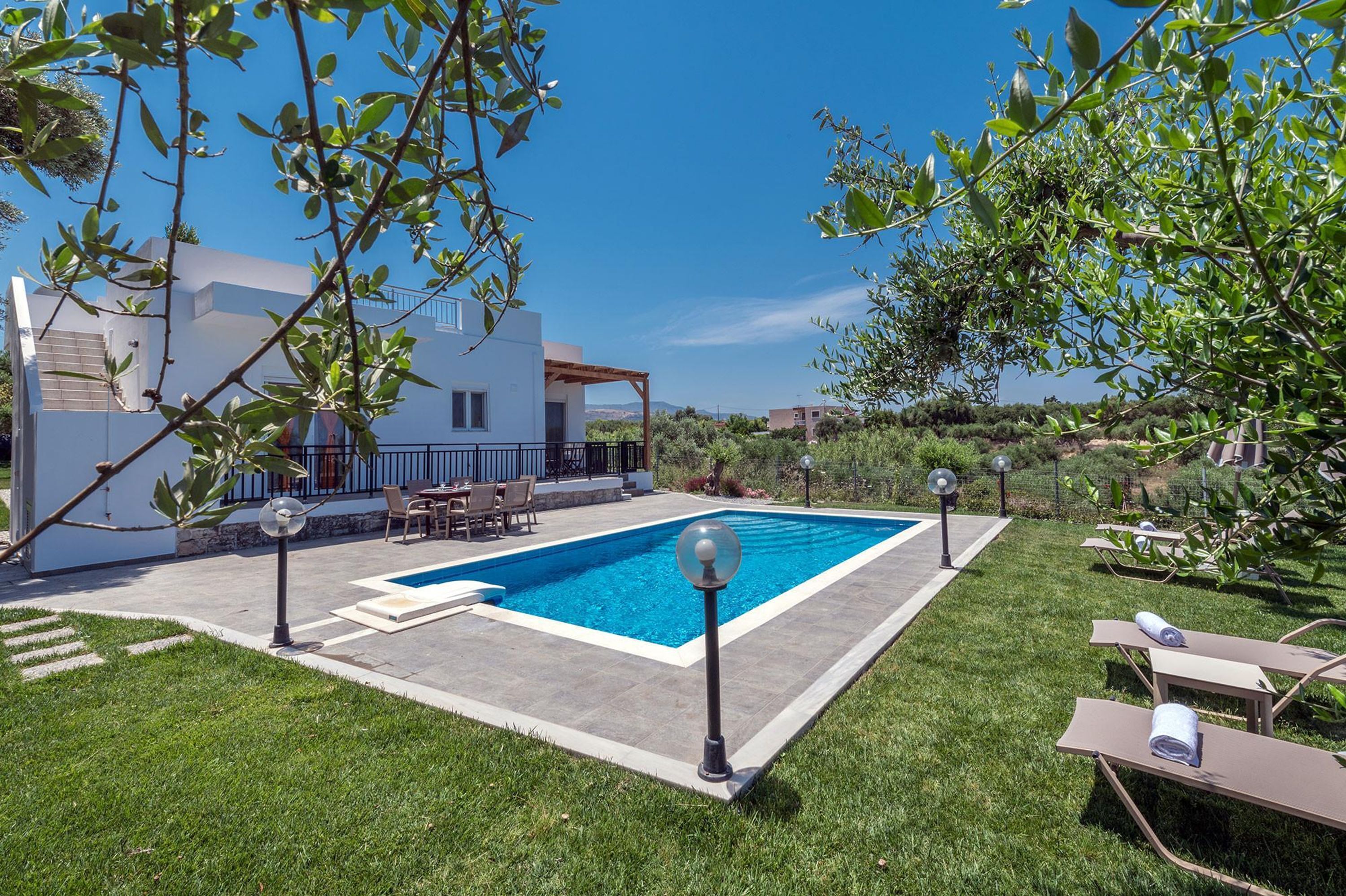 Una casa moderna con piscina, mobiliario exterior y un césped bien cuidado.