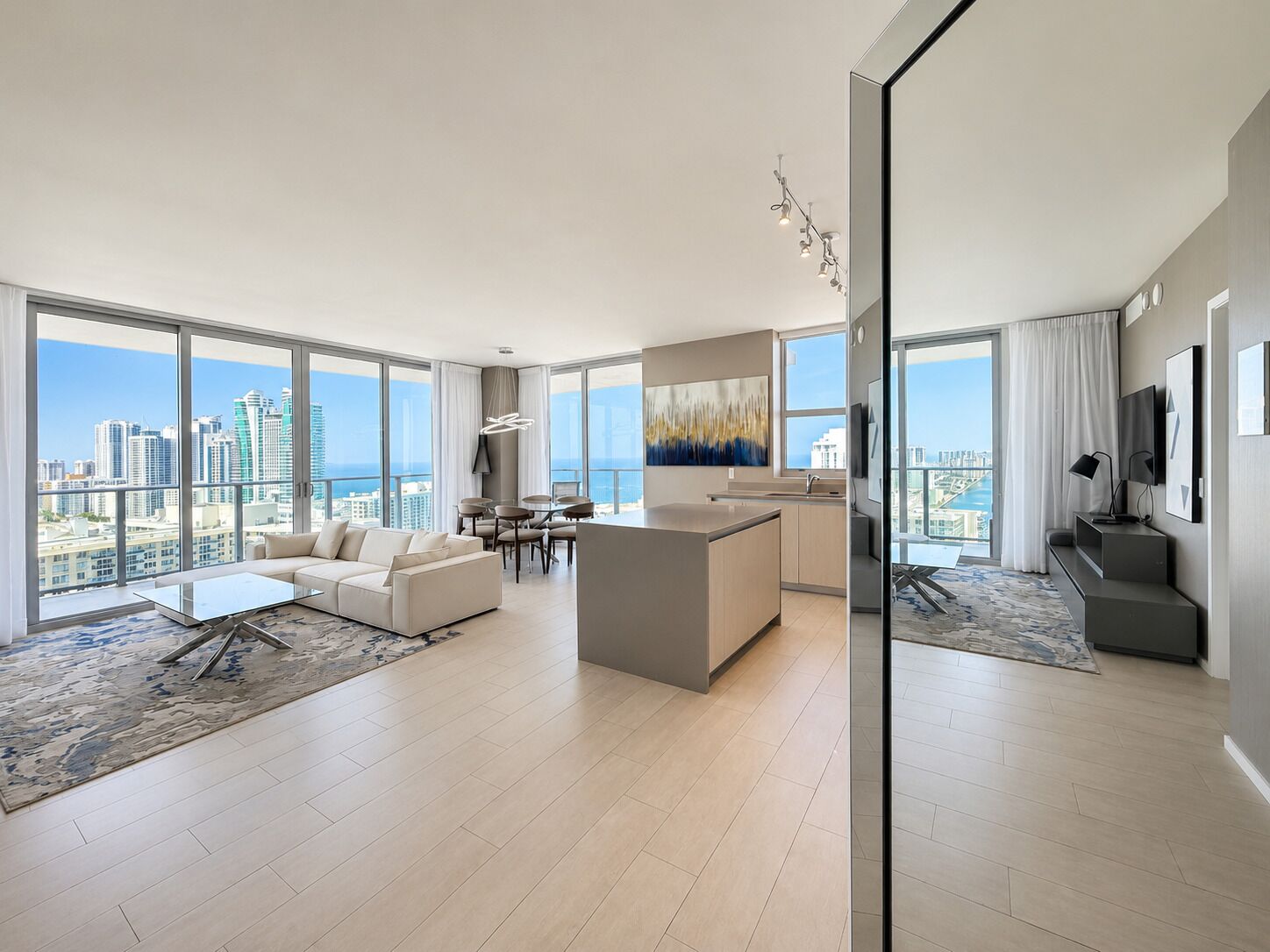 A modern apartment with a living area, kitchen, and dining space, featuring large windows and a city view.