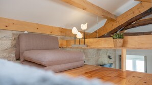 A cozy room with a wooden ceiling, a stone wall, a cushioned bench, and a hanging plant. - Bonjardim City Flats - Top Floor (Porto)