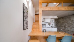 A modern kitchen with white cabinets, a stone wall, and a wooden dining table with two chairs. - Bonjardim City Flats - Top Floor (Porto)
