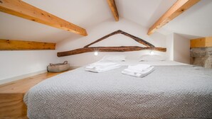 A bedroom with a sloped ceiling, wooden beams, a bed with white linens, and a stone wall. - Bonjardim City Flats - Top Floor (Porto)