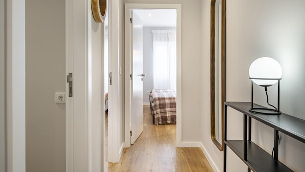 A hallway with a bed in the background, a mirror, and a lamp on a console table. - Nomad s Family - 2bdr Sunny Firmeza (Porto)