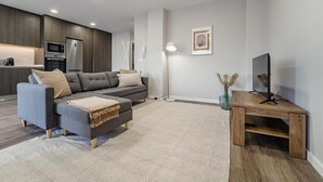 Een moderne woonkamer met een grijze bank, een houten salontafel en een tv op een houten dressoir.