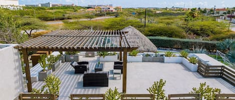 A rooftop terrace with a pergola, seating area, and potted plants.