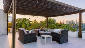 Eine Außenpatio mit Korbmöbeln, einer Pergola und Topfpflanzen.