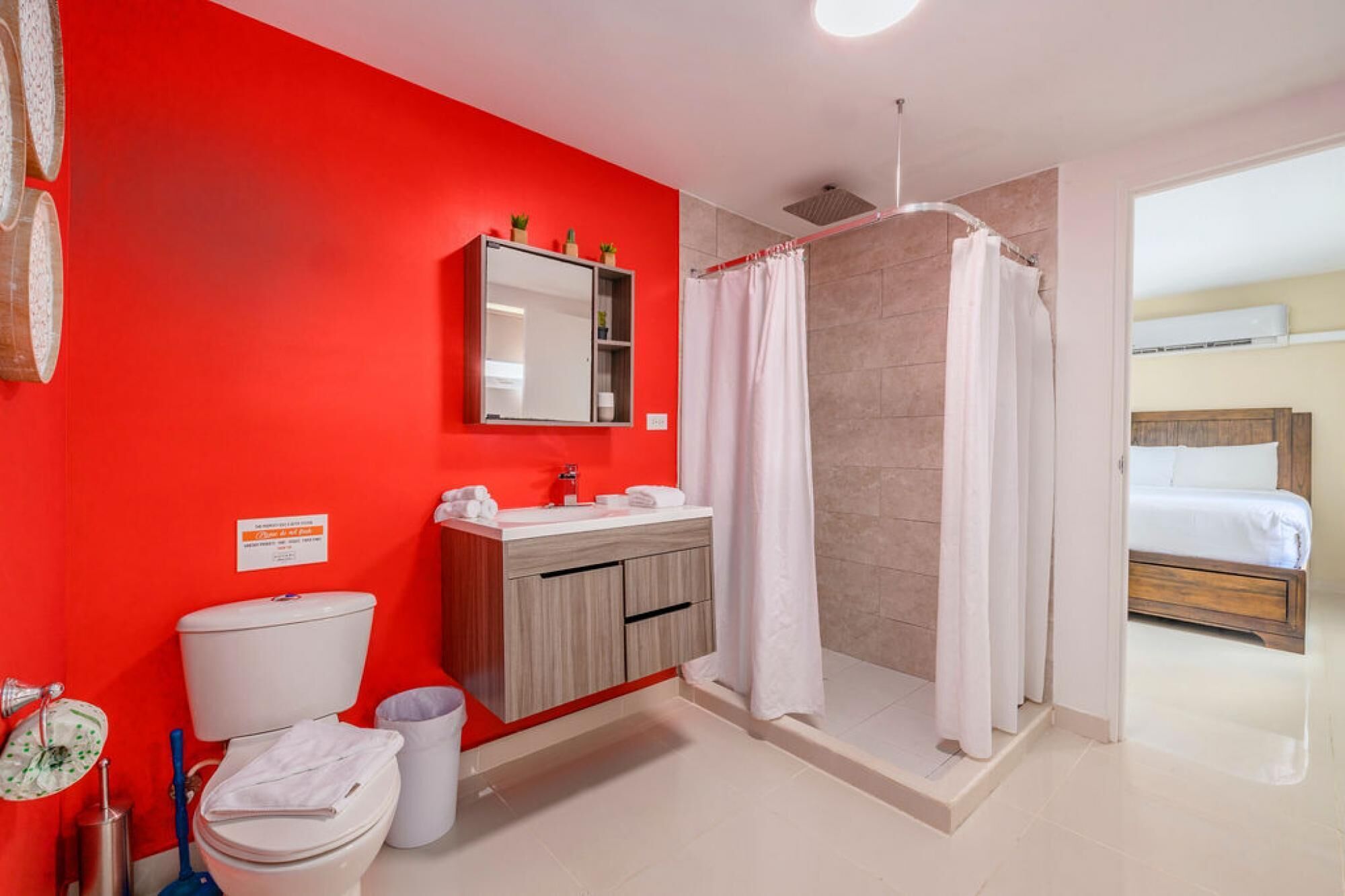 Un baño con pared roja, lavabo blanco, inodoro y zona de ducha.