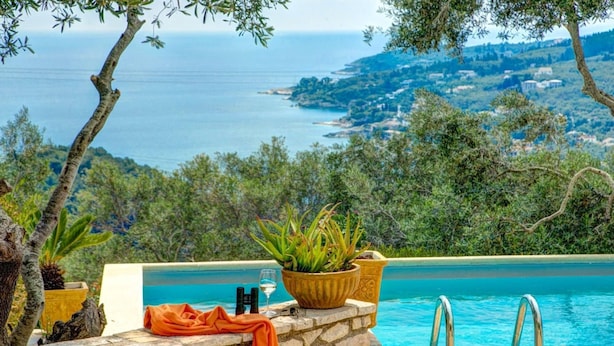 A poolside view with a stone wall, a potted plant, a glass, and a towel. - Kalliope Villa - Classic Modern With a Splash of Glam (Paxos)