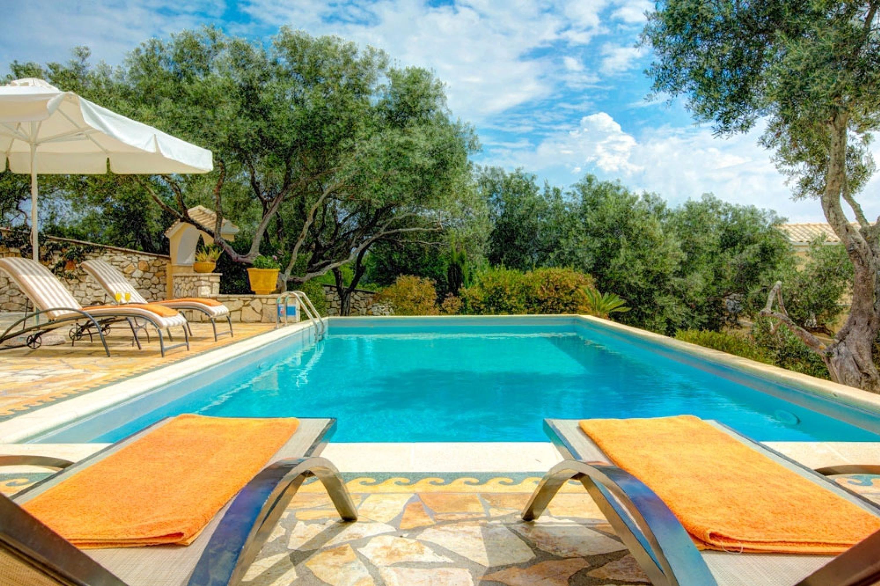 Una piscina con lettini e ombrelloni, circondata da alberi e muri in pietra.