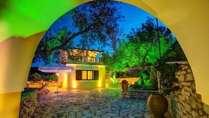 A stone-paved courtyard with a small building, a large vase, and a tree. - Kalliope Villa - Classic Modern With a Splash of Glam (Paxos)