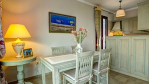 Een eetgedeelte met een tafel, stoelen, een vaas met bloemen, een lamp en een ingelijste foto.