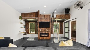 Una sala de estar moderna con chimenea, un televisor de pantalla plana grande y una zona de entrepiso con escalera.