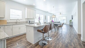 A spacious kitchen with a central island, bar stools, and a dining area with a table and chairs. - BRAND NEW CONSTRUCTION NEAR DOWNTOWN & SMF AIRPORT (Sacramento)