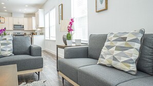 A modern living room with grey sofas, a coffee table, and a kitchen in the background. - BRAND NEW CONSTRUCTION NEAR DOWNTOWN & SMF AIRPORT (Sacramento)