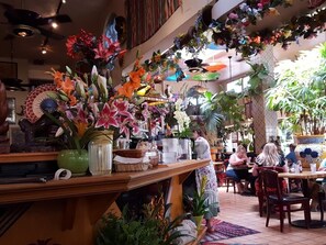 Ein Restaurant mit vielfältiger Bepflanzung und Blumen, Holzmöbeln und einem Fliesenboden.