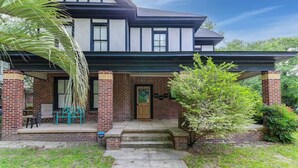 Ein zweistöckiges Haus mit Backsteinfassade, einer Veranda mit Bank und einem kleinen Baum im Vorgarten.