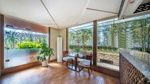 Ein moderner Essbereich mit einem Glastisch und Stühlen, umgeben von großen Fenstern mit Blick auf Grünflächen und einen Bambusgarten.