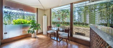 A modern interior with a dining area, large windows, and a view of greenery.