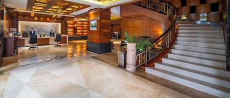 A hotel lobby with a reception desk, a staircase, and a check-in counter.