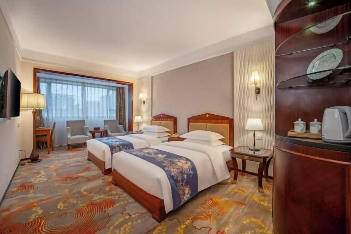 Una habitación de hotel con dos camas, un escritorio, una silla, un televisor y una ventana con cortinas.