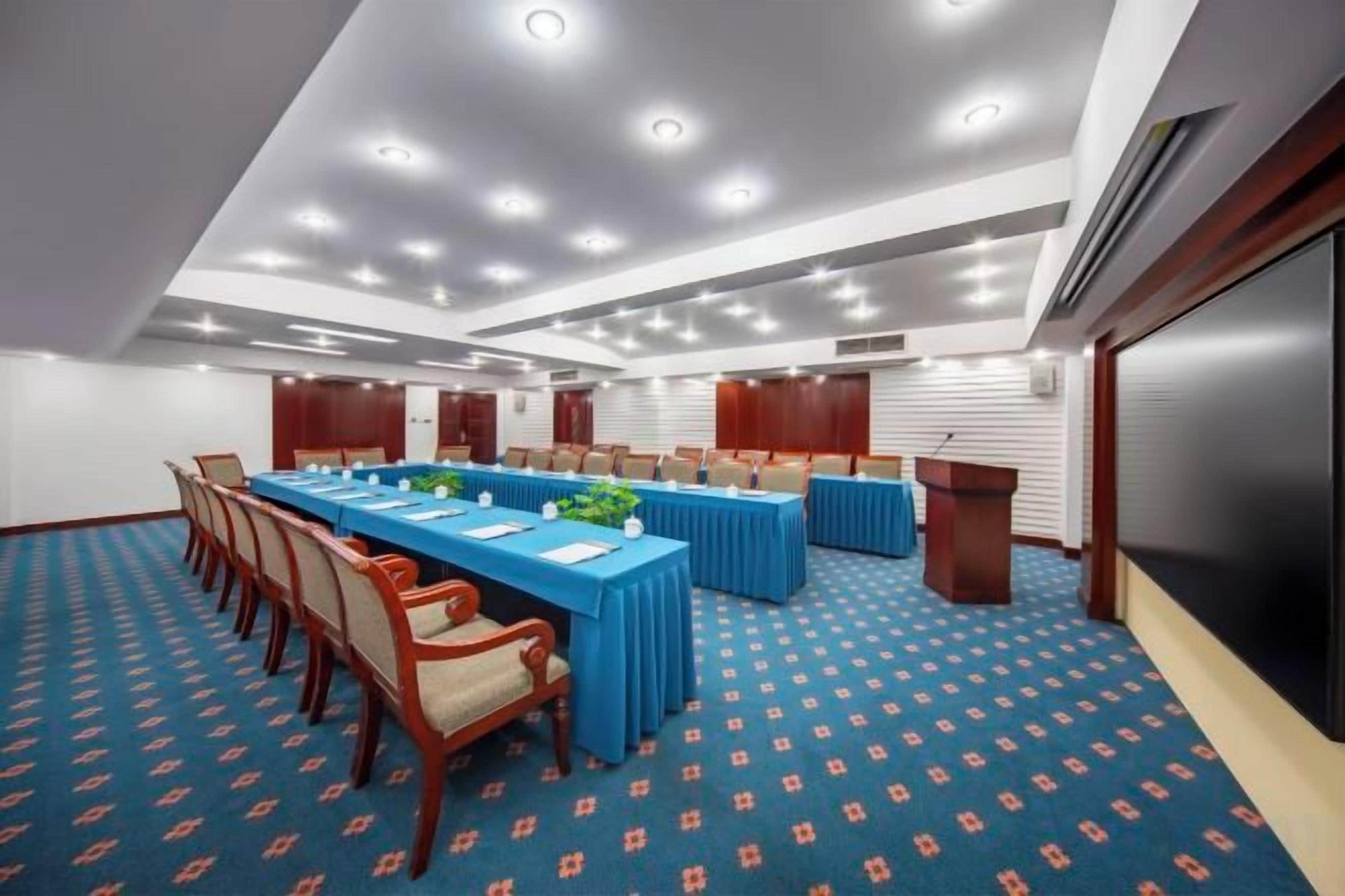 Sala de conferência com uma mesa comprida, cadeiras e um pódio.