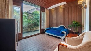 Ein Zimmer mit Holzboden, einem großen Fenster, einem blauen Sofa, einem beigen Sessel und einem Fernseher.