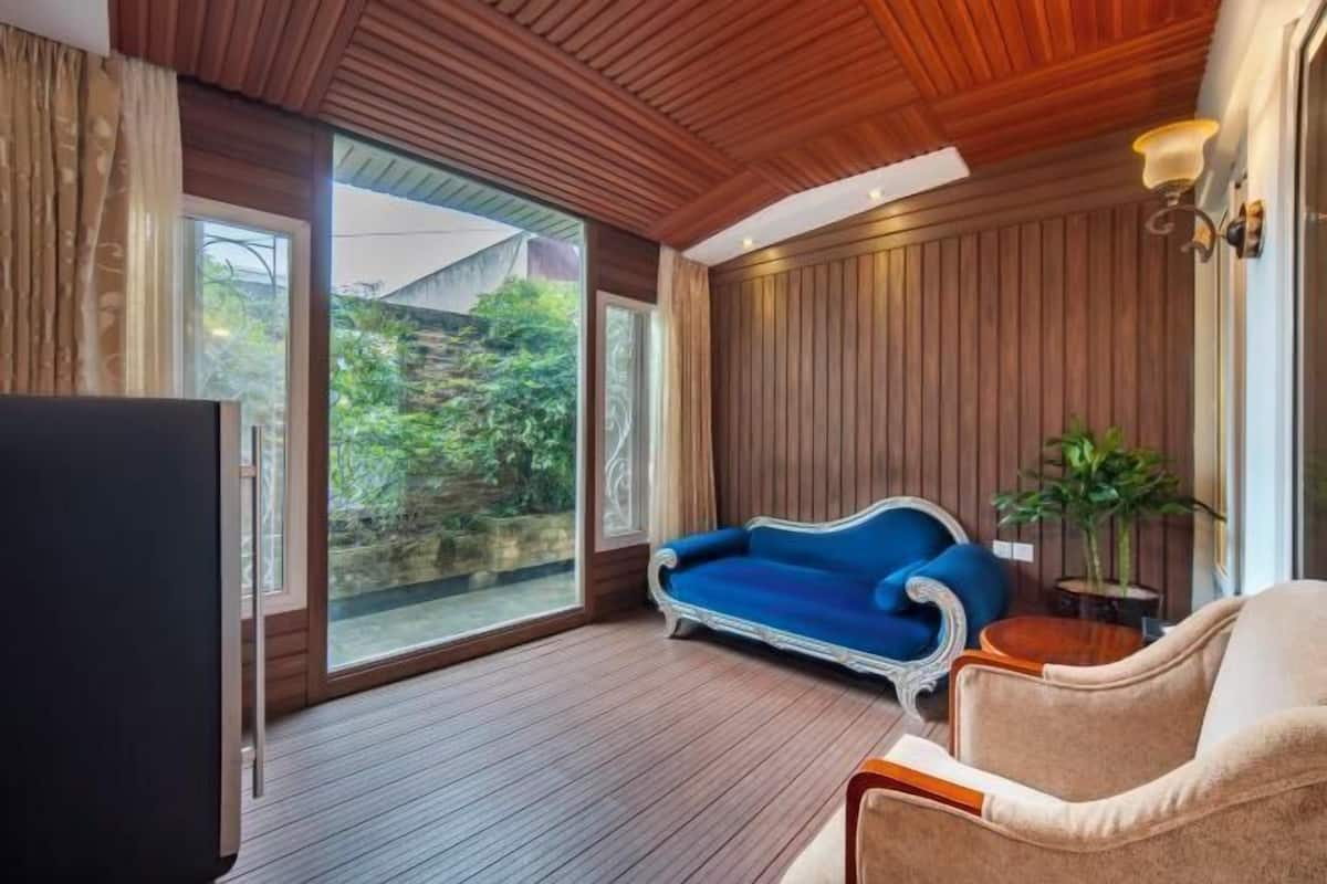 Una habitación con techo de madera, un ventanal grande, un sofá azul, un sillón color beige y un televisor.