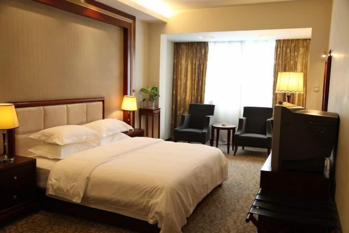 Una habitación de hotel con una cama grande, dos sillas, una mesita y un televisor.