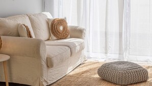 A cozy living room with a beige sofa, a round woven throw pillow, and a knitted pouf on a textured rug. - Villa Soleil by Acasadascasas (Mafra)